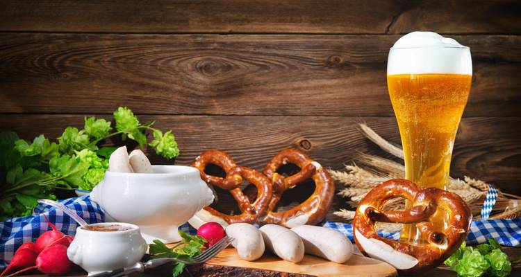 Traditionele Beierse snack opstelling met pretzels, witte worsten en een hoog glas bier op rustieke houten achtergrond