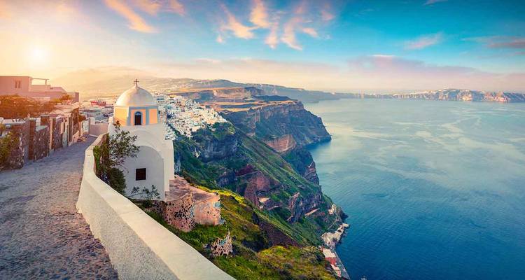Sentier du coucher de soleil le long du rebord de la caldeira de Santorin avec une chapelle blanchie à la chaux surplombant la mer Égée.