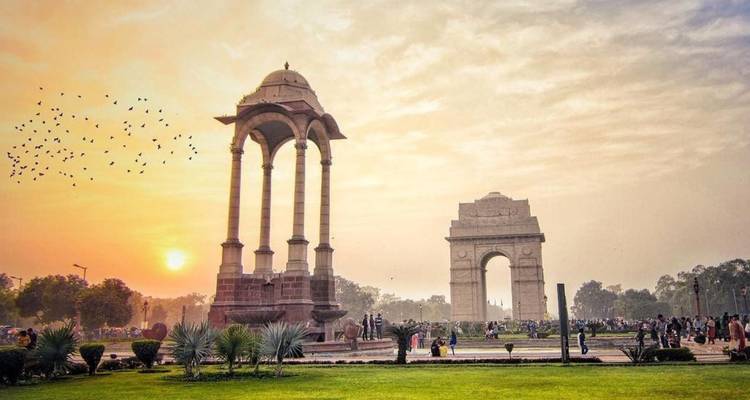 India Gate und Überdachungsdenkmal bei Sonnenuntergang mit Menschenmengen und Vögeln, die sich gegen den Himmel abzeichnen
