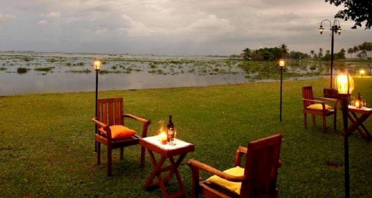 Gemütliches Outdoor-Dining-Setup mit Laternen und Holzstühlen mit Blick auf ruhige Gewässer bei Abenddämmerung.
