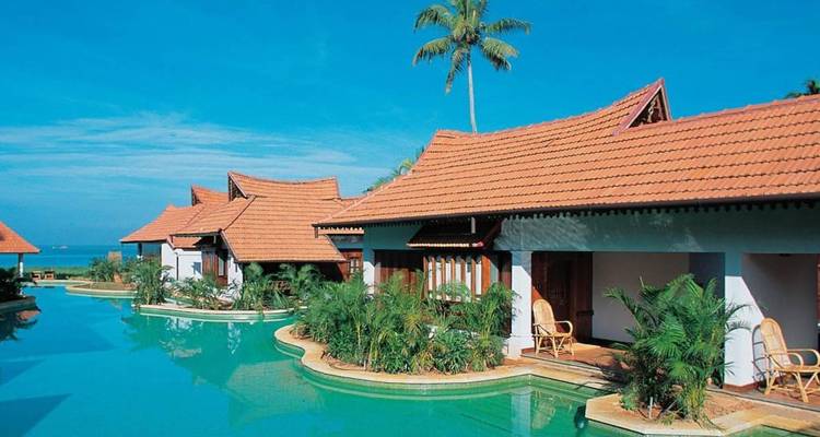 Luxuriöse Wasserfront-Villen mit Ziegeldächern, die einen türkisfarbenen Pool im Lagunen-Stil unter klarem blauem Himmel umgeben.