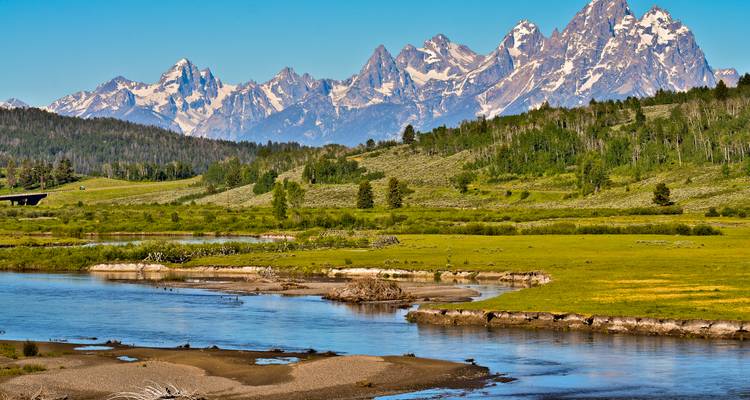 Picos nevados de la cordillera Grand Teton elevándose sobre un río serpenteante y un valle exuberante.