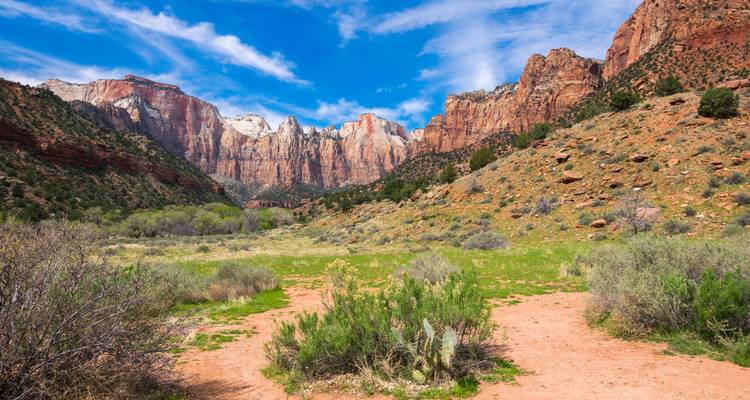 Amplio valle enmarcado por imponentes acantilados de roca roja bajo un cielo azul vívido y nubes tenues.