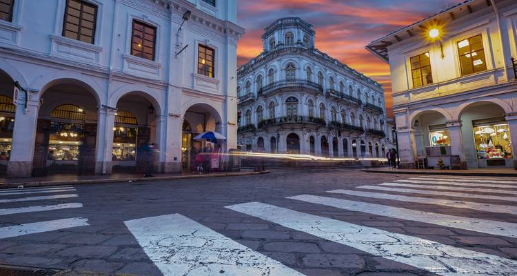 Historische koloniale straat in Quito bij zonsondergang met gloeiende hemel, wazige lichtsporen en voetgangers onder booggewelven.