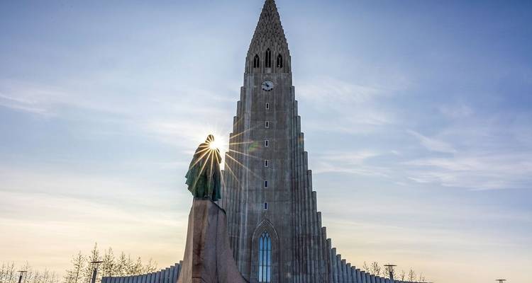 Hallgrímskirkja church soars into a clear sky as sunlight creates a starburst behind the Leif Erikson statue.