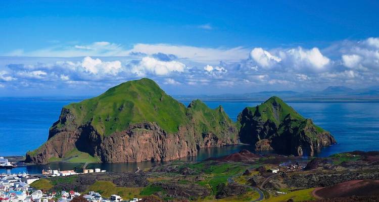 Green volcanic islands rise from deep blue sea with scattered clouds overhead, seen from a high viewpoint.