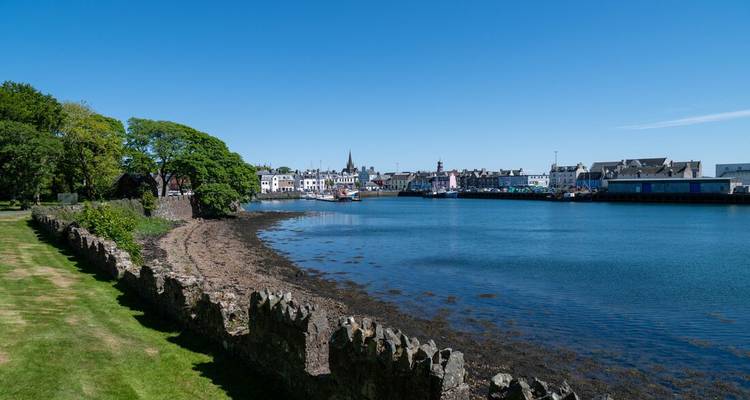 A quiet harbor town lines a sheltered blue bay under a clear summer sky.