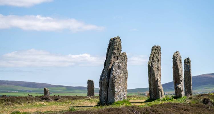 Ancient standing stones rise from open moorland under a clear blue Orkney sky.