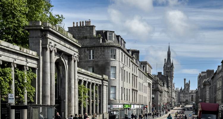 Granite buildings and archways line busy Union Street in central Aberdeen under patchy clouds.