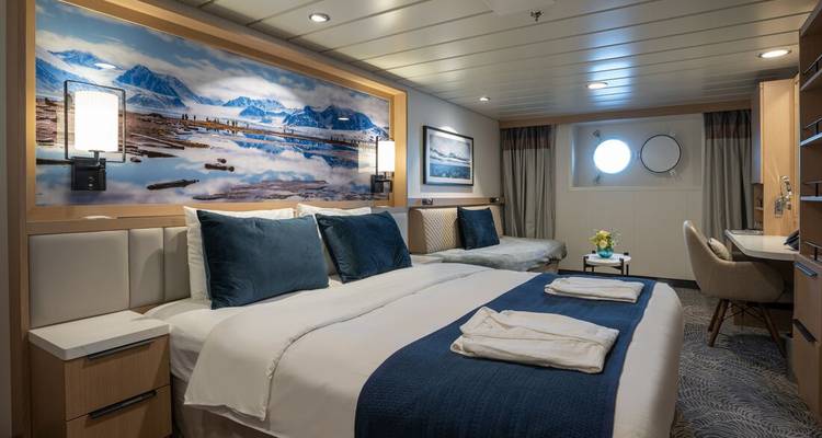 Camarote de crucero moderno con cama grande, obras de arte de paisajes polares y ventanas de ojo de buey.