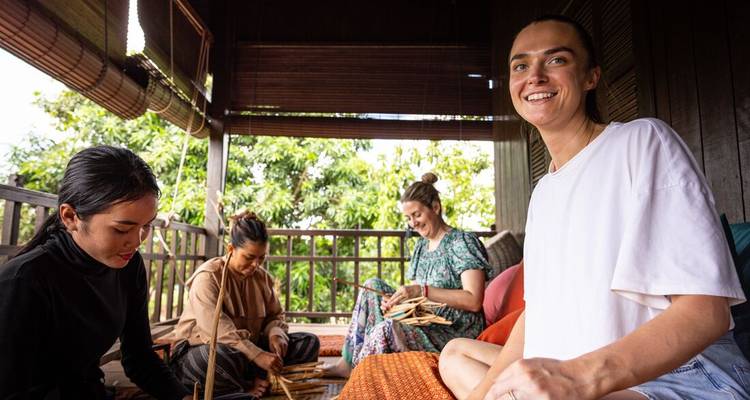 Visiteurs apprenant le tissage traditionnel sur une terrasse en bois ombragée entourée de verdure