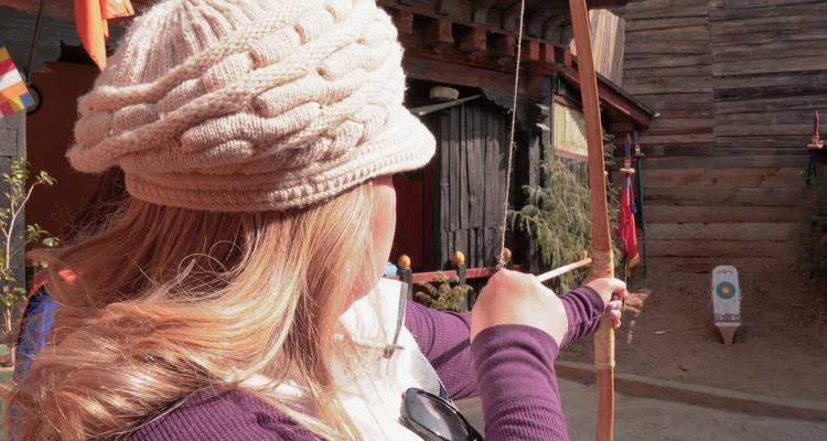 Une femme vise avec un arc traditionnel lors d'un entraînement de tir à l'arc sur un terrain bhoutanais en planches de bois.