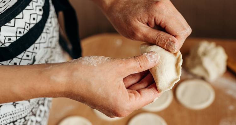 Gros plan de mains façonnant une boulette de pâte sur une table farinée avec des ronds de pâtisserie en arrière-plan.