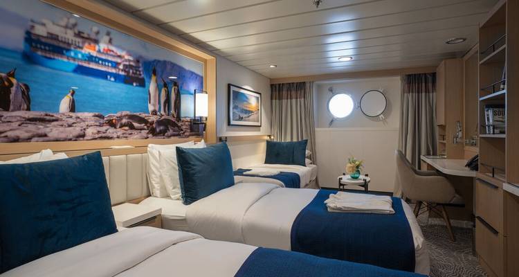 Modernes Doppelzimmer an Bord eines Expeditionsschiffes mit blauen Akzenten, Pinguin-Kunstwerken und Bullaugen.