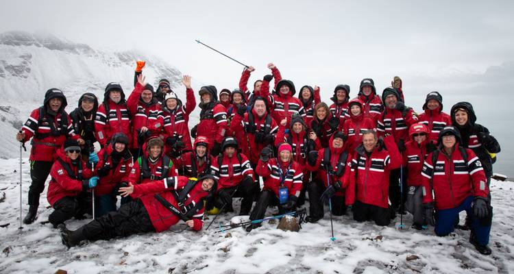Große Expeditionsgruppe in einheitlichen roten Parkas, die sich an der verschneiten Küste der Antarktis fotografieren lässt.
