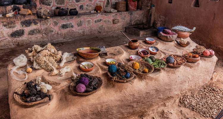 A rustic workbench displays baskets of natural dyes, wool and plants used in traditional weaving.