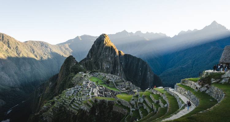 Iconic postcard vista of Machu Picchu at dawn with light rays breaking over Andean peaks and emerald terraces.