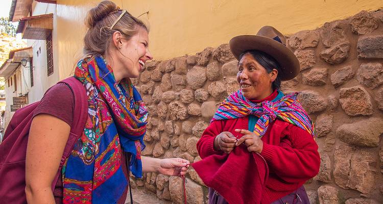 Traveler laughing with a local Andean woman spinning yarn beside stone wall