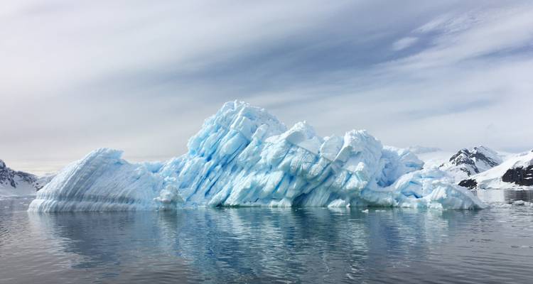 Strahlend blau getönter Eisberg, der ruhig in antarktischen Gewässern unter einem gedämpften Himmel treibt.