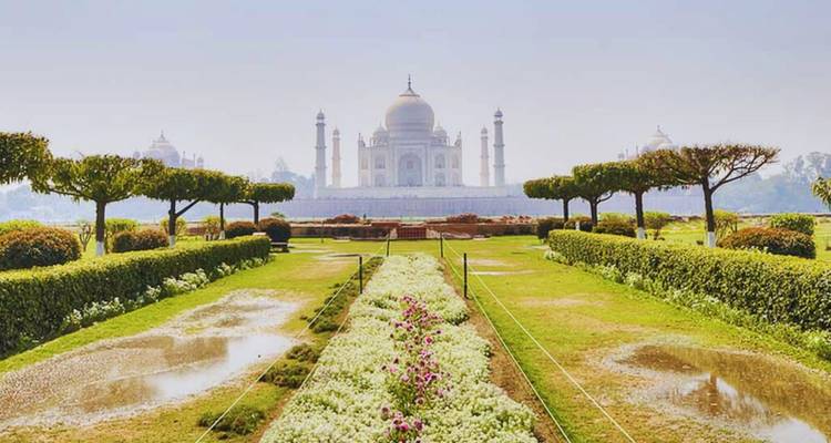 Vue emblématique du Taj Mahal à travers les bassins réfléchissants et les haies taillées après une pluie récente.