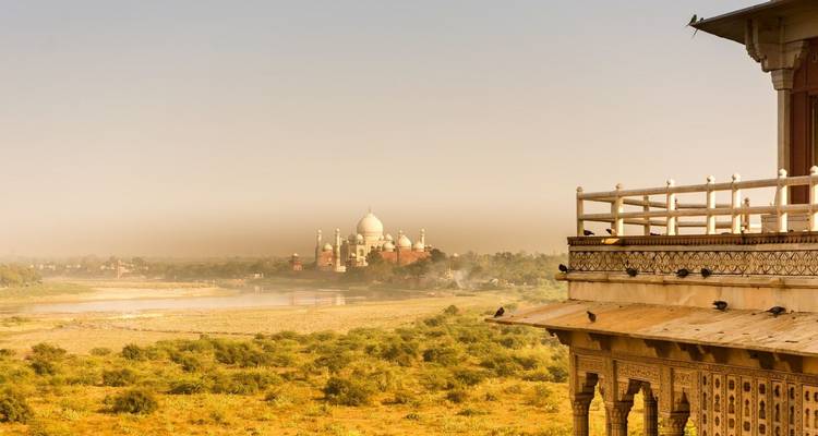 Le Taj Mahal lointain s'élève de la rive opposée de la rivière Yamuna sous un ciel brumeux.