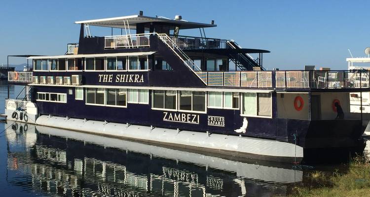Moored Zambezi river houseboat 'The Shikra' reflected in calm water at dock