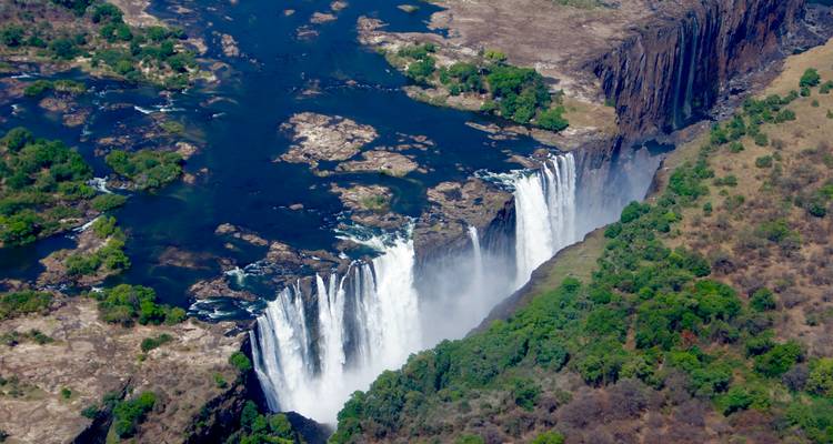 Aerial perspective of mighty Victoria Falls cascading into narrow gorge surrounded by greenery