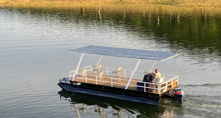 Small pontoon boat with roof glides across calm lake dotted with tree stumps