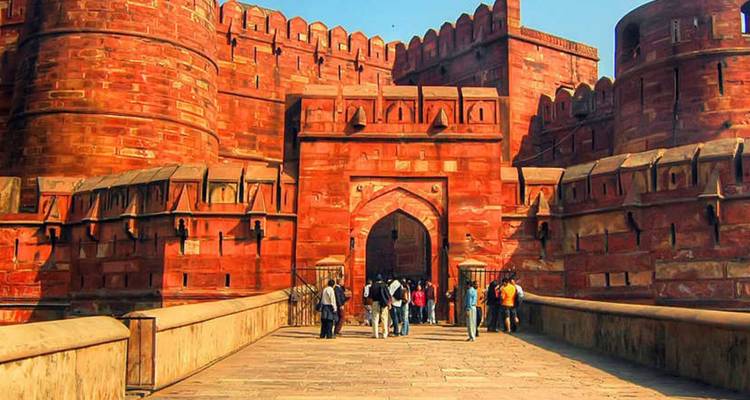 Les touristes traversent le pont de pierre en entrant dans les massives murailles rouges du Fort d'Agra.