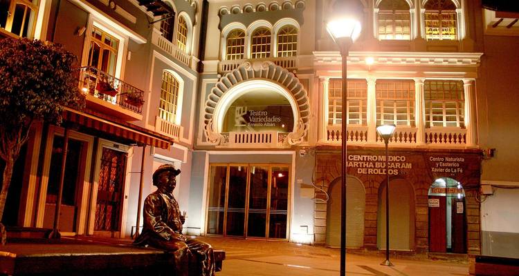 Una fachada de teatro histórico y edificios cercanos están cálidamente iluminados en una calle nocturna desierta.