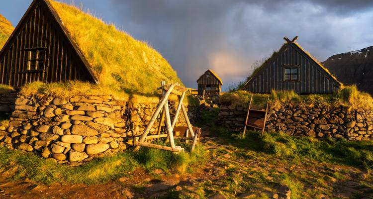 Cluster van traditionele campings met zoden daken en stenen muren die glanzen in het gouden avondlicht onder dramatische luchten.