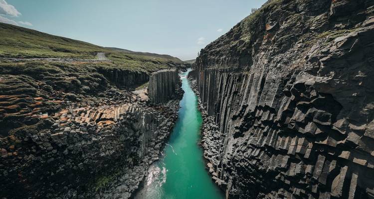 Un fleuve turquoise s'écoule à travers un canyon aux colonnes de basalte profond sous des cieux dégagés.