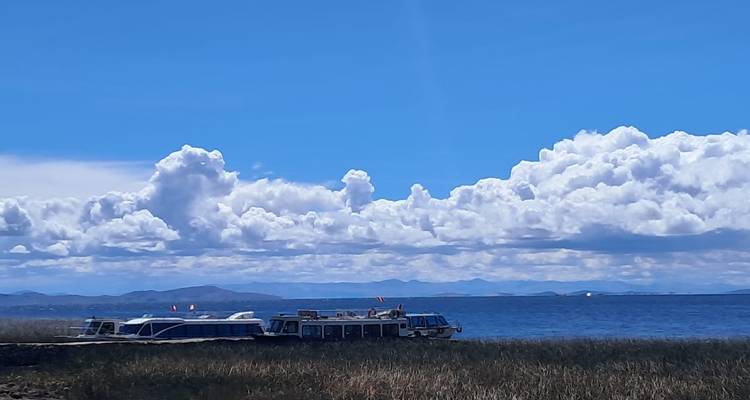 Les bateaux de passagers reposent sur les eaux bleu profond du lac Titicaca sous un vaste ciel parsemé de nuages cumulus spectaculaires.