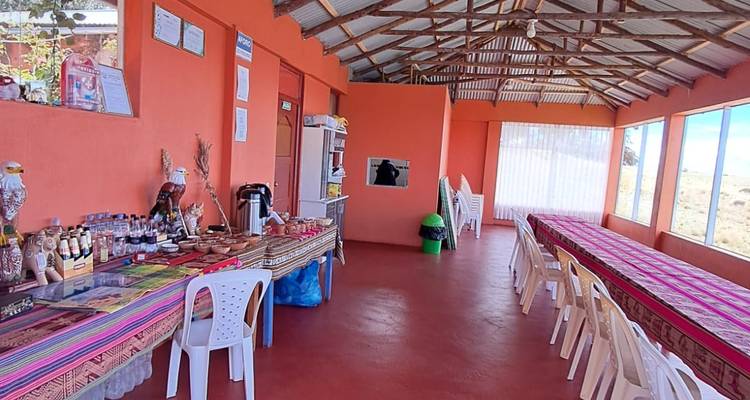 Salle à manger communautaire d'un orange vif avec de longues tables recouvertes de textiles andin colorés et une exposition de produits locaux.