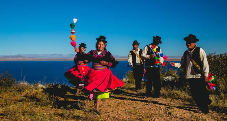 Les habitants en tenue traditionnelle éclatante exécutent une danse animée sur un promontoire qui surplombe l'étendue bleu profond du lac Titicaca.