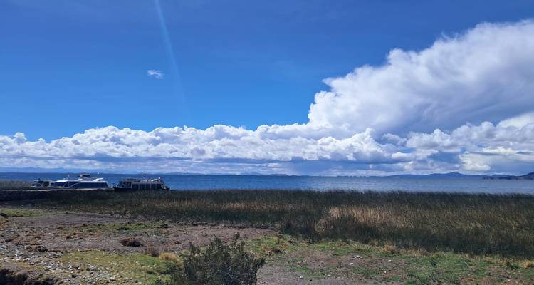 Vue panoramique sur un vaste lac encadré par des roseaux et des formations nuageuses spectaculaires s'étendant sur les crêtes lointaines de la Cordillère des Andes.