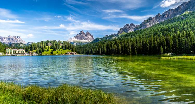 Lac alpin cristallin entouré d'une dense forêt de pins avec des sommets tachetés de neige se reflétant dans ses eaux.