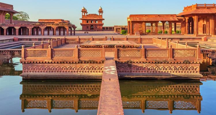 Reflecting pool and ornate pavilions inside Fatehpur Sikri complex at sunset.