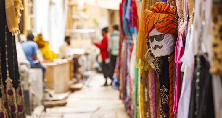 Colorful market alley with hanging textiles and a quirky turban-wearing puppet head sporting sunglasses.