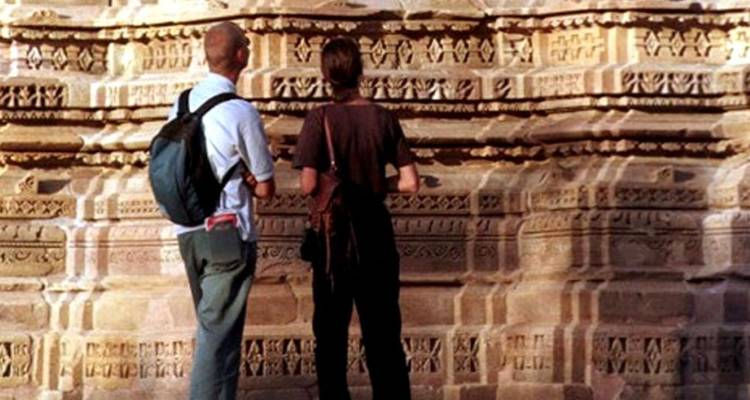 Two tourists study detailed stone carvings on an ancient temple wall.