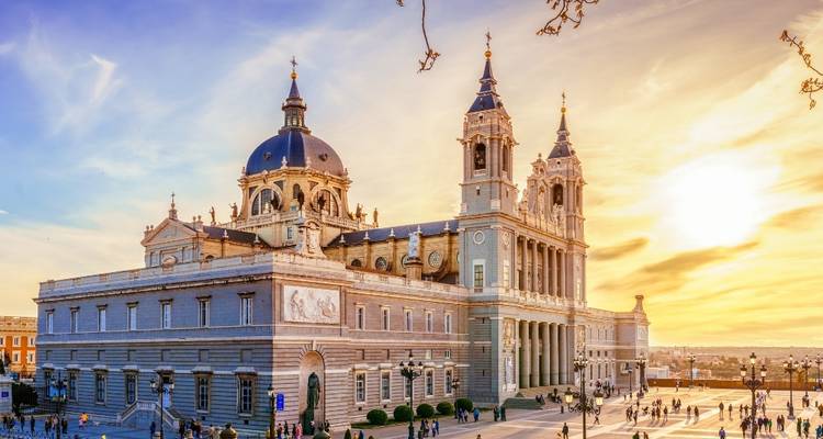 Die Almudena-Kathedrale im goldenen Licht des Sonnenuntergangs mit Besuchern, die über den weitläufigen Vorplatz verstreut sind.