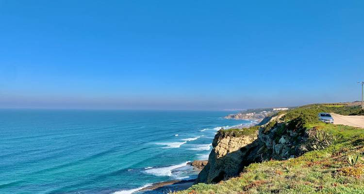 Weite Sicht auf eine zerklüftete Küstenlinie mit klarem blauen Ozean und einer Straße auf der Klippe unter wolkenlosem Himmel.