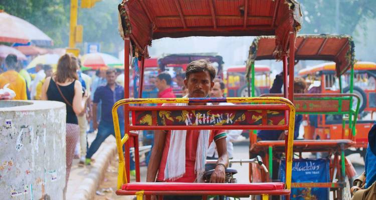 Geschäftige Straße in Delhi mit bunten Fahrradrikschas und Fahrgästen, die sich durch den Verkehr bewegen.