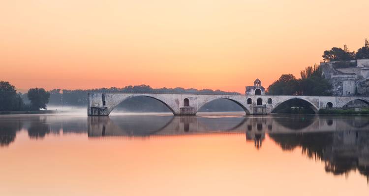 Serene sunrise over Pont Saint-Bénezet bridge reflecting in the still Rhône River at Avignon.