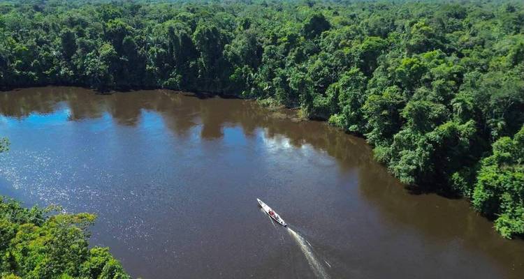 Vue aérienne par drone d'un large fleuve brun serpentant à travers l'épaisse forêt tropicale amazonienne avec un petit bateau à moteur.