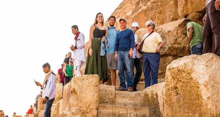 Tourists climb limestone blocks on the side of a Giza pyramid, posing for photos.
