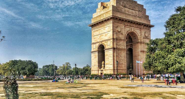 El monumento de arenisca India Gate se alza en un parque abierto con visitantes paseando alrededor.