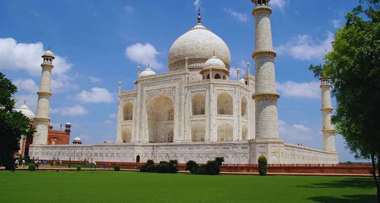 El pristino Taj Mahal blanco con cuatro minaretes se alza bajo un cielo azul vívido sobre césped verde.