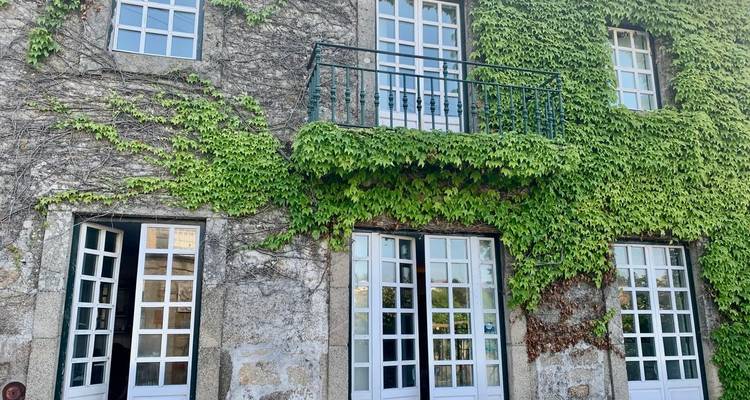 Façade de bâtiment en pierre entièrement recouverte de lierre vert luxuriant avec fenêtres françaises blanches et balcon