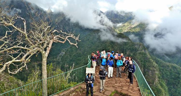 Large hiking group gathers on a cloud-topped viewpoint terrace high above verdant mountains